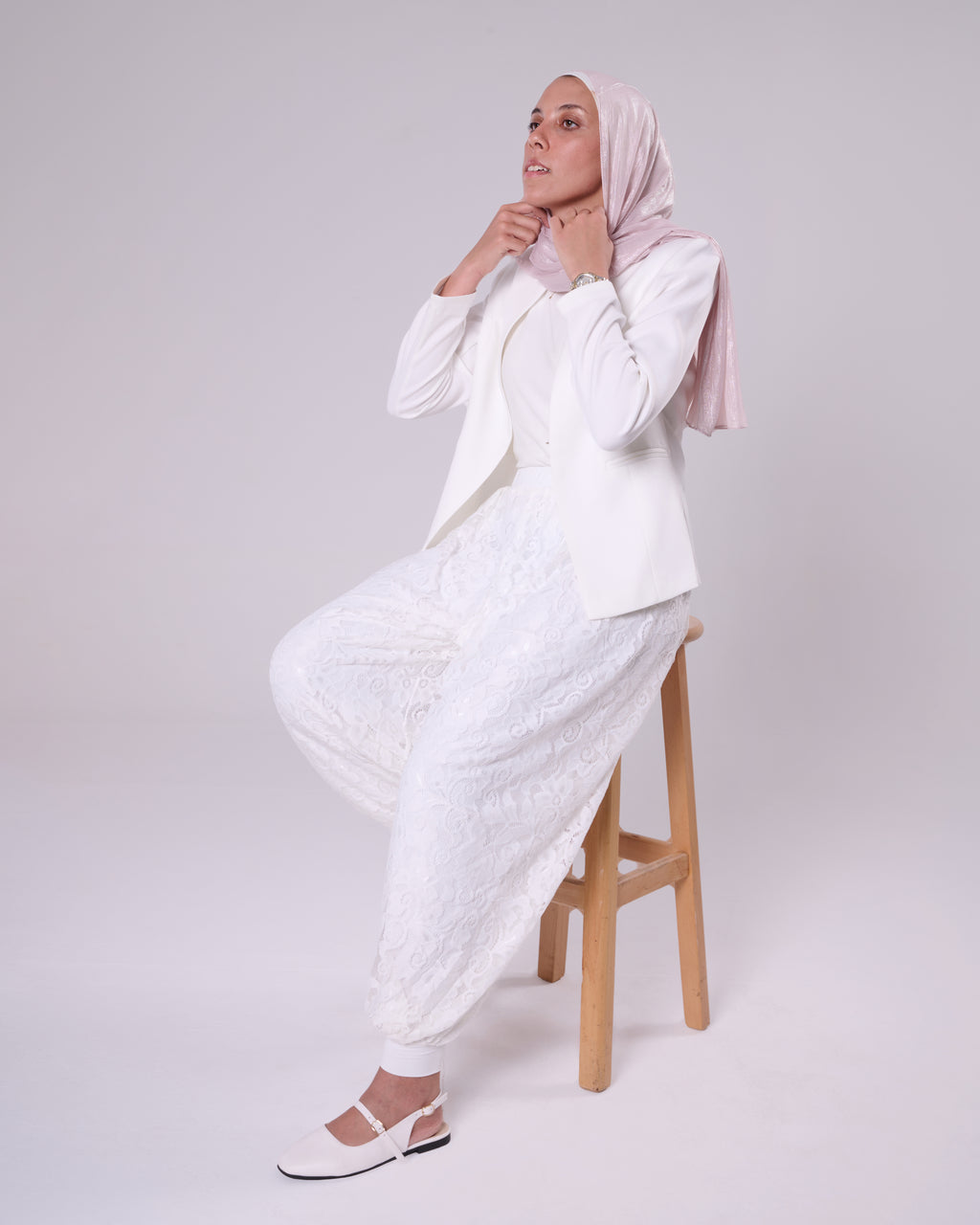 Floral Pants by DAJ, White, seated, dynamic pose — balloon-leg lace pants showing the elastic ankle cuff and drape of the fabric.